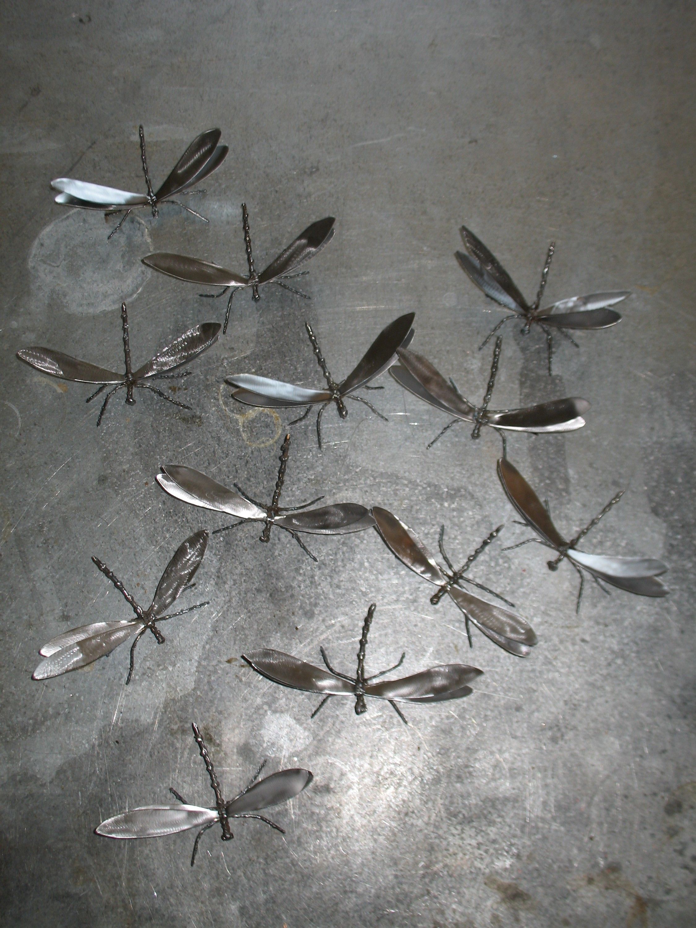 Polished steel dragonflies laid out across a scratched steel table, each with four leaf-shaped wings and a beaded body