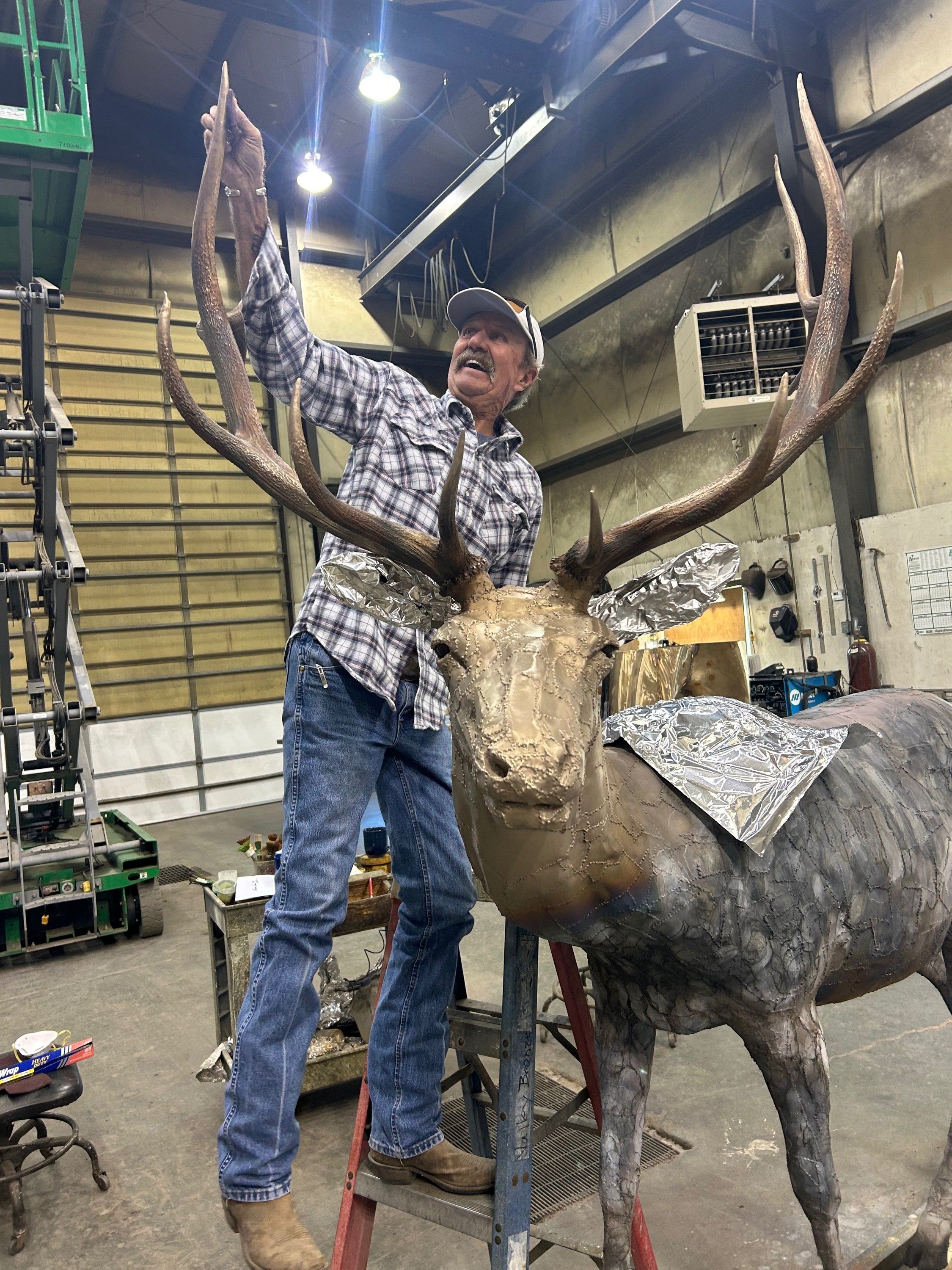 Russ Lamb on a ladder working on the life-size bronze bull elk in his studio