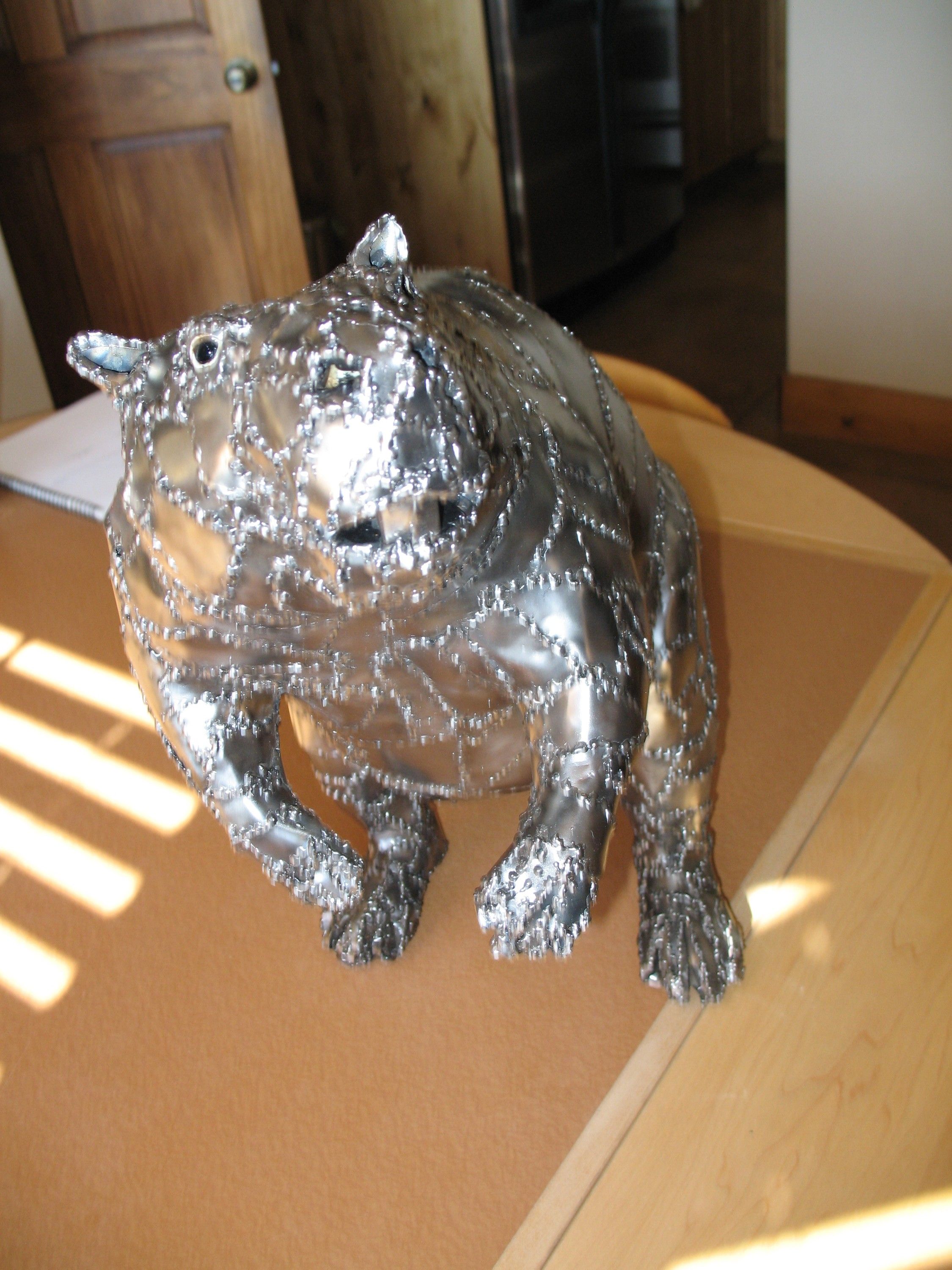 The steel beaver on all fours on the table, its polished panels and stitched weld seams catching the light