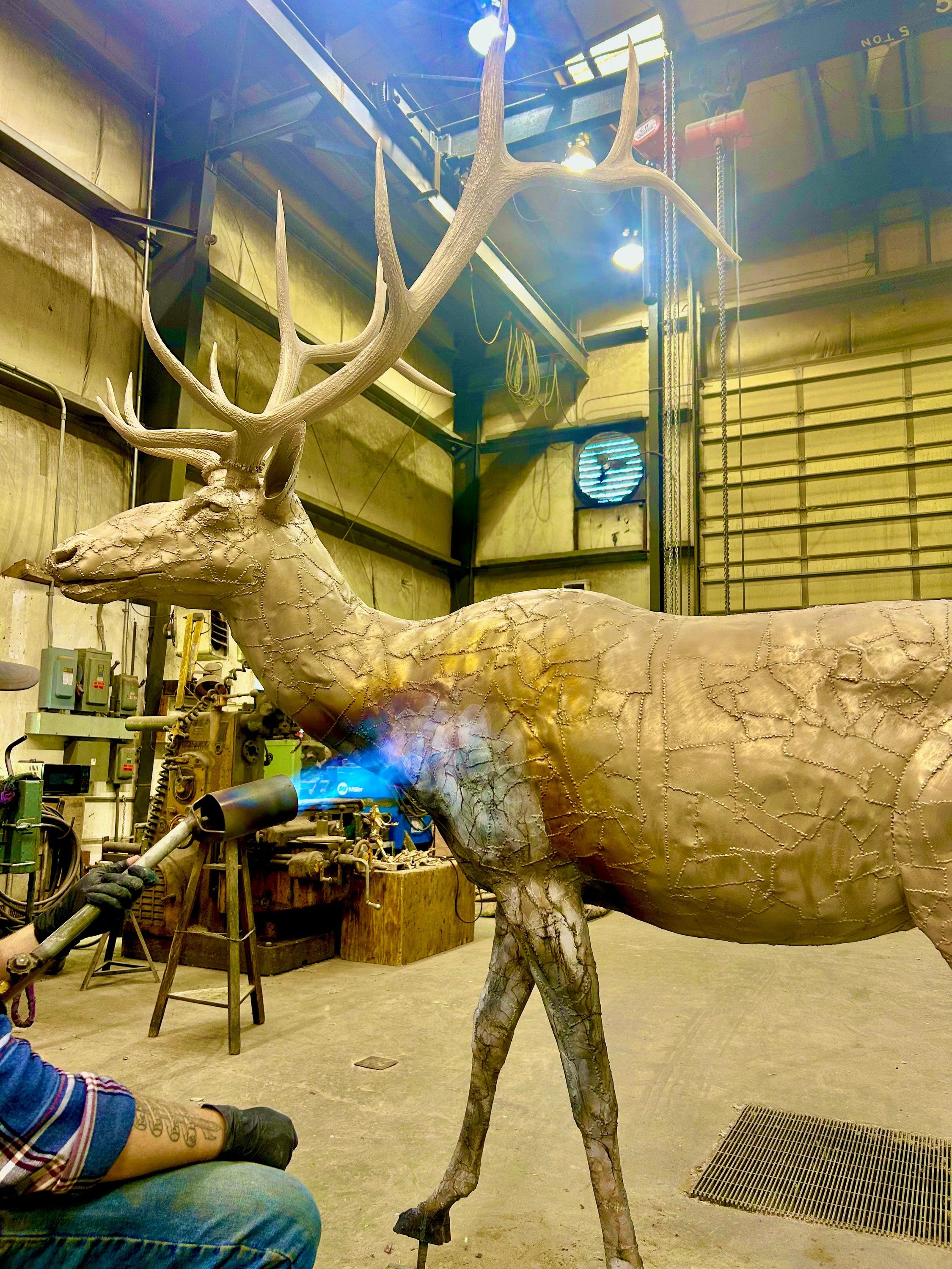 A torch flame playing across the bronze bull elk's shoulder as the patina is applied