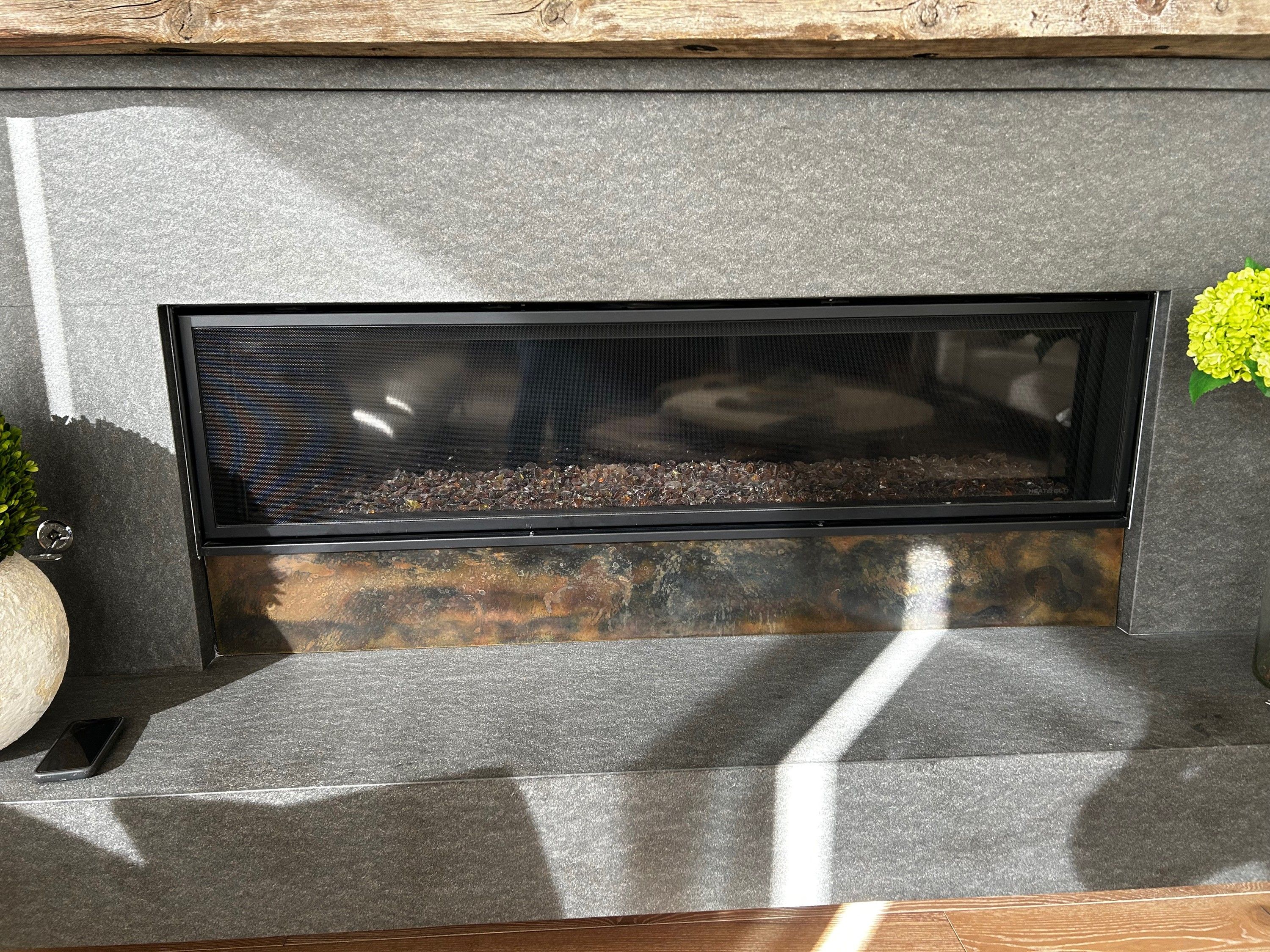 The firebox from closer in, the patina steel panel below the glass showing its mottled rust, blue and cream surface across the width of the opening