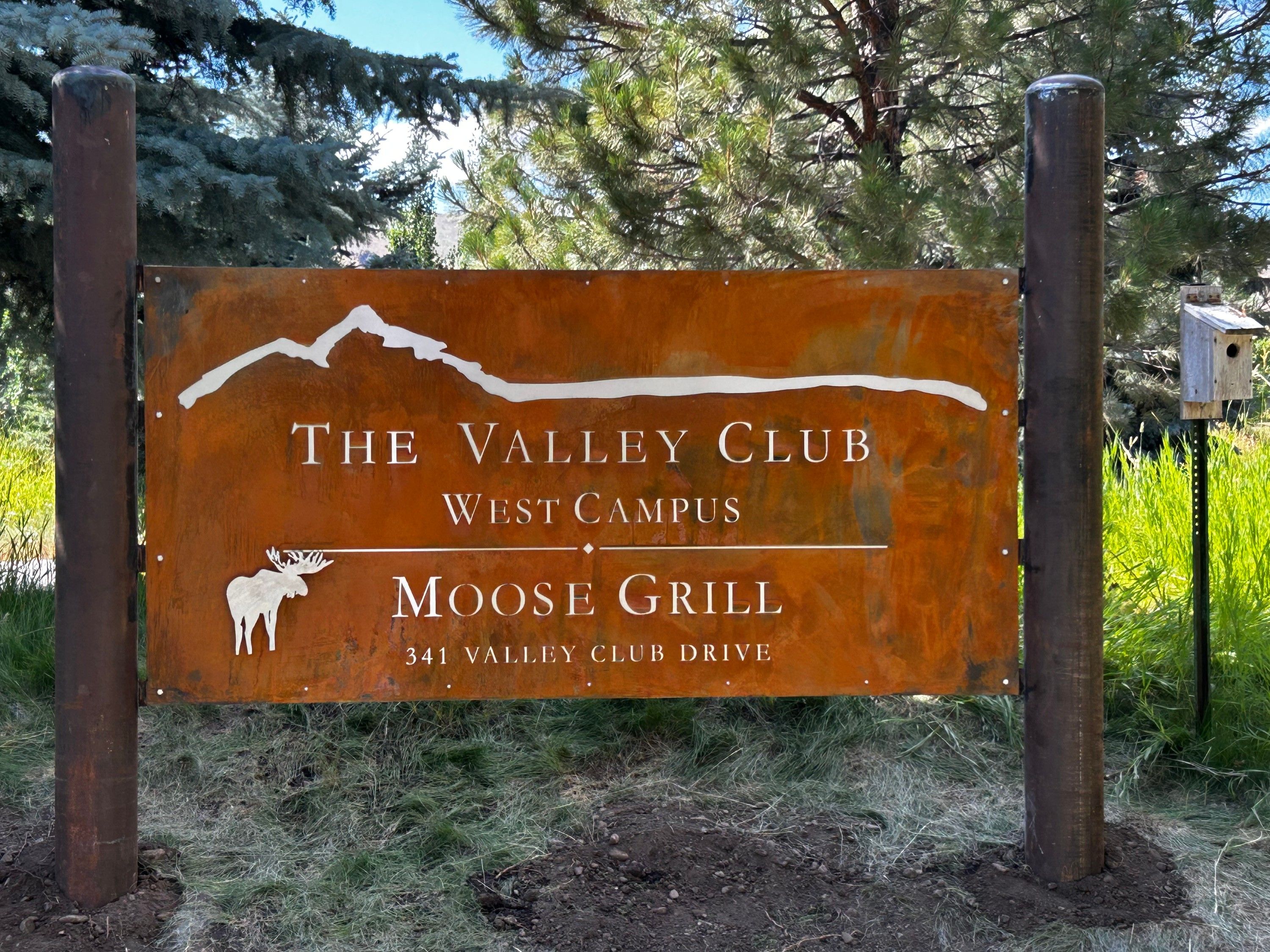 The Valley Club Moose Grill sign on timber posts among the trees