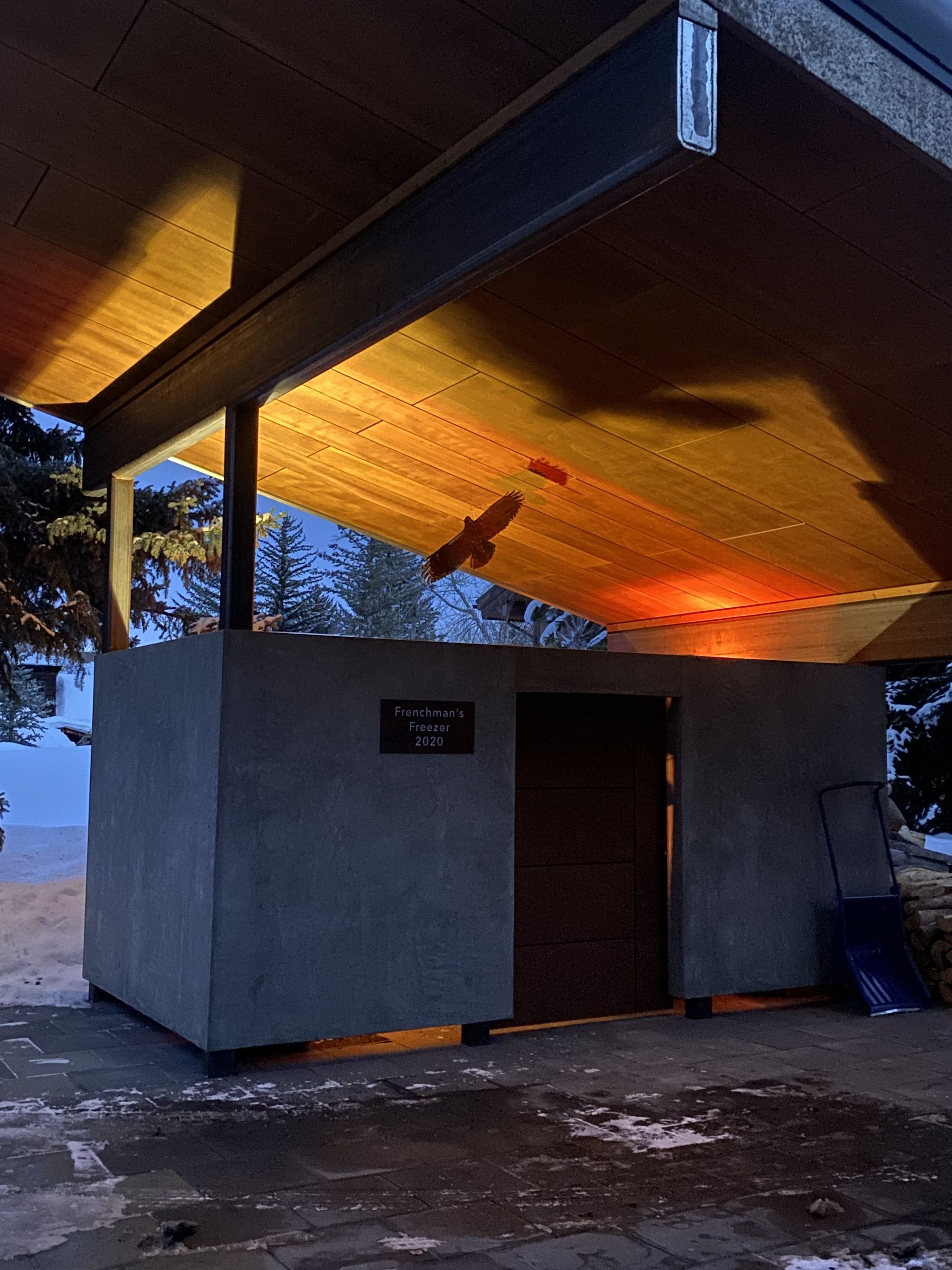 The steel hawk in flight pose beneath a glowing carport ceiling at dusk
