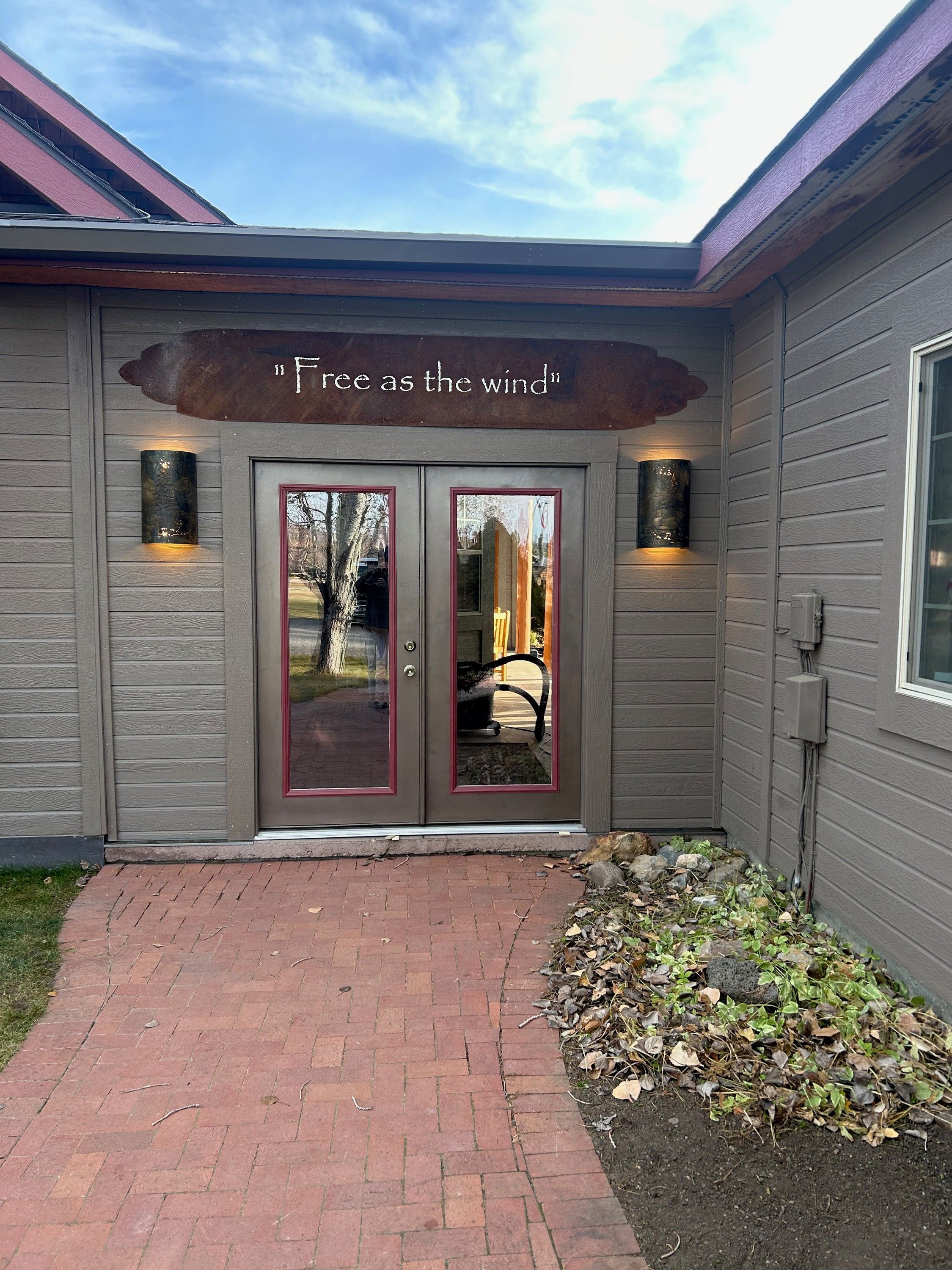 A steel sign reading Free as the wind mounted above a pair of glass doors, with a cylindrical patina steel sconce lit on either side