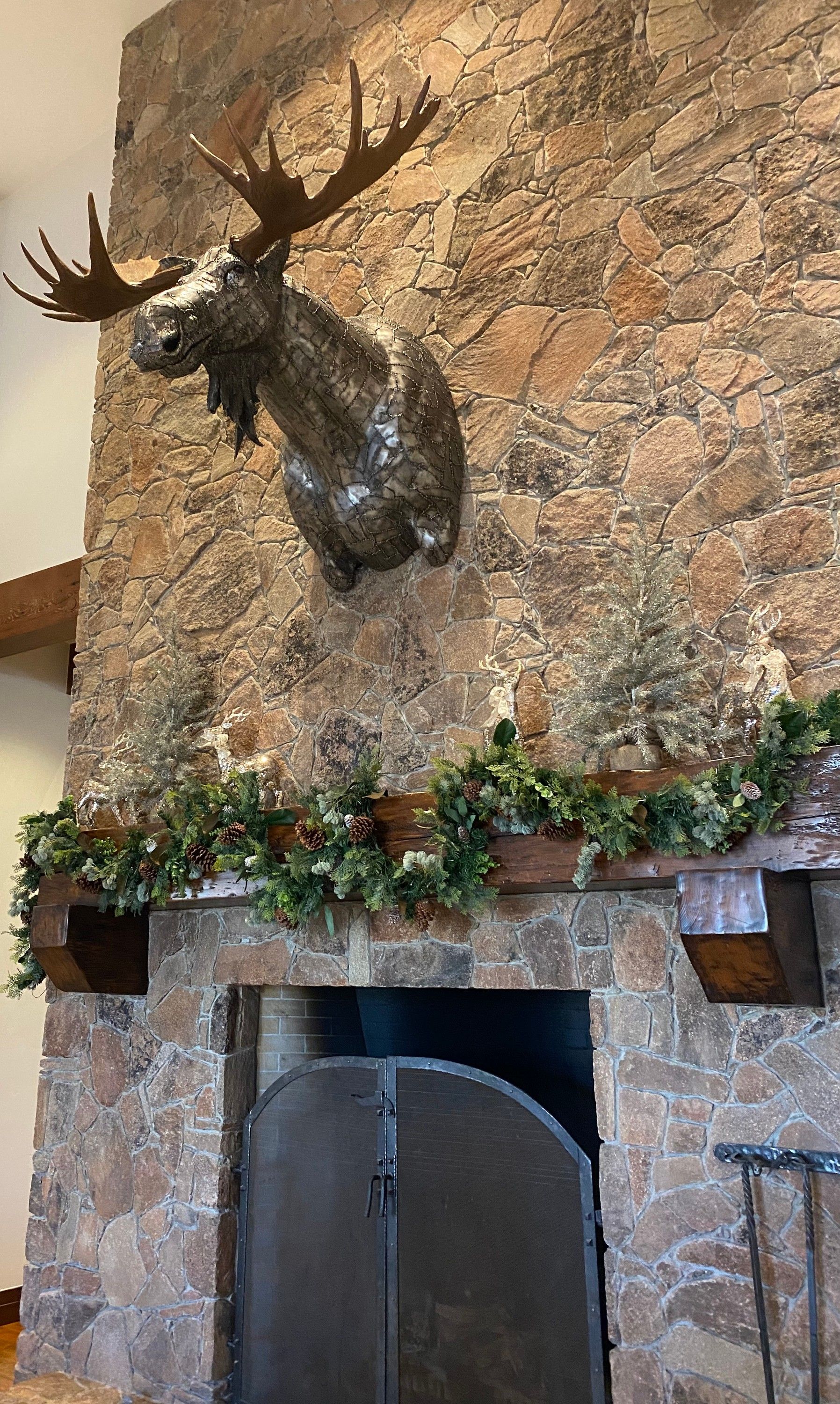 The moose head high on a stone chimney breast above a fireplace, a green garland running along the timber mantel below