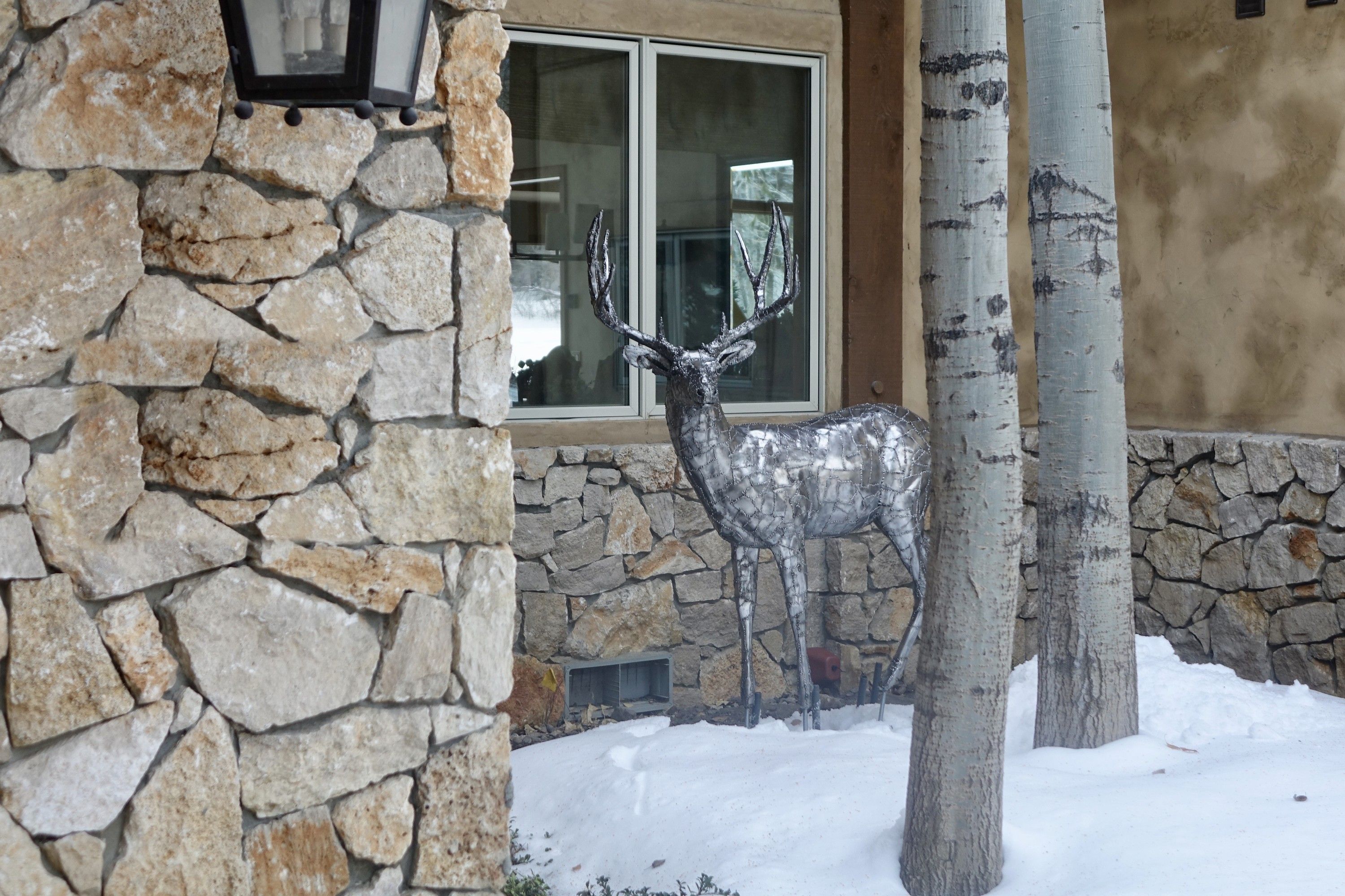 The steel buck standing in snow beside the house, a stone pier and a lantern in the foreground