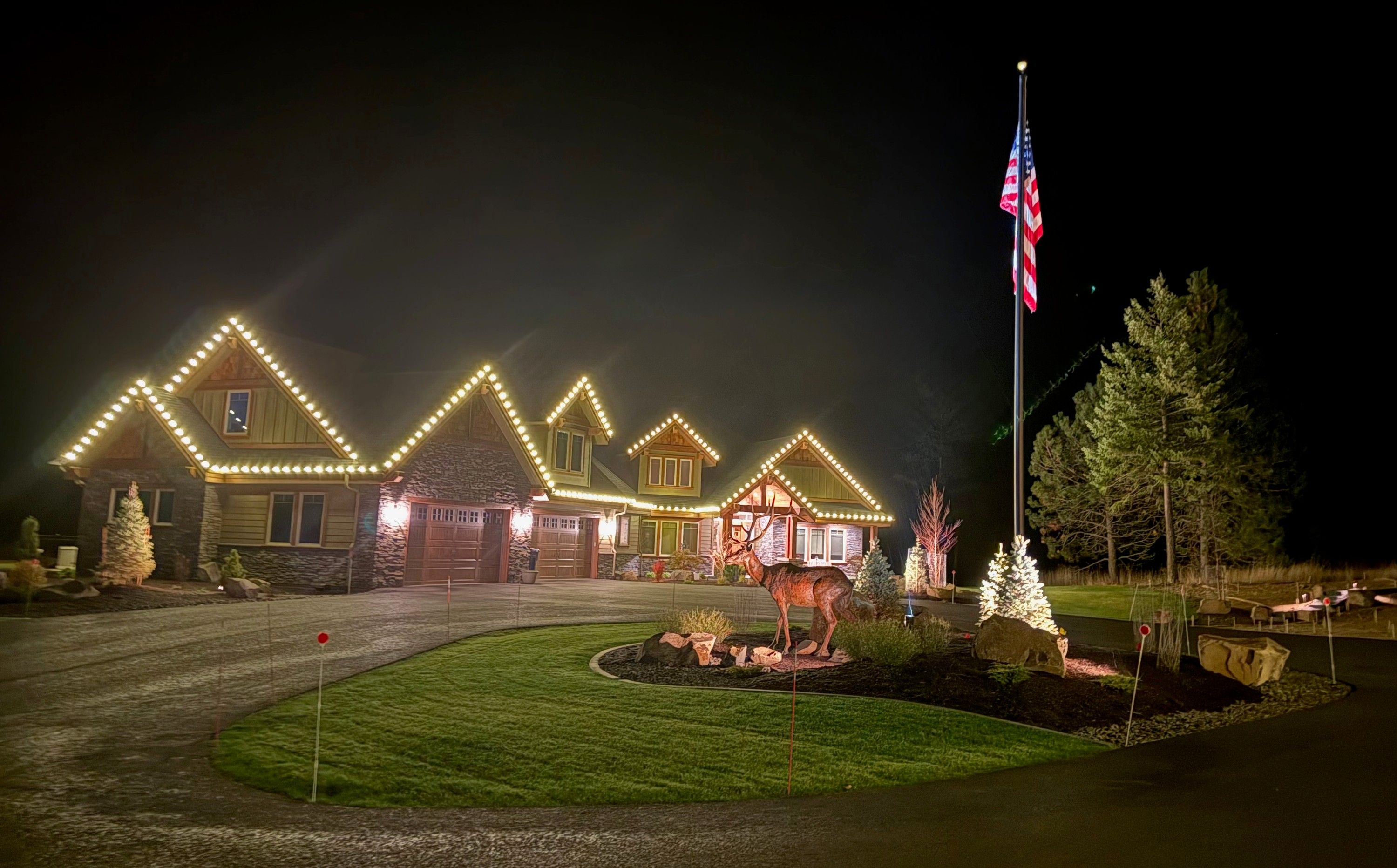 The bronze bull elk at night in front of a house strung with holiday lights