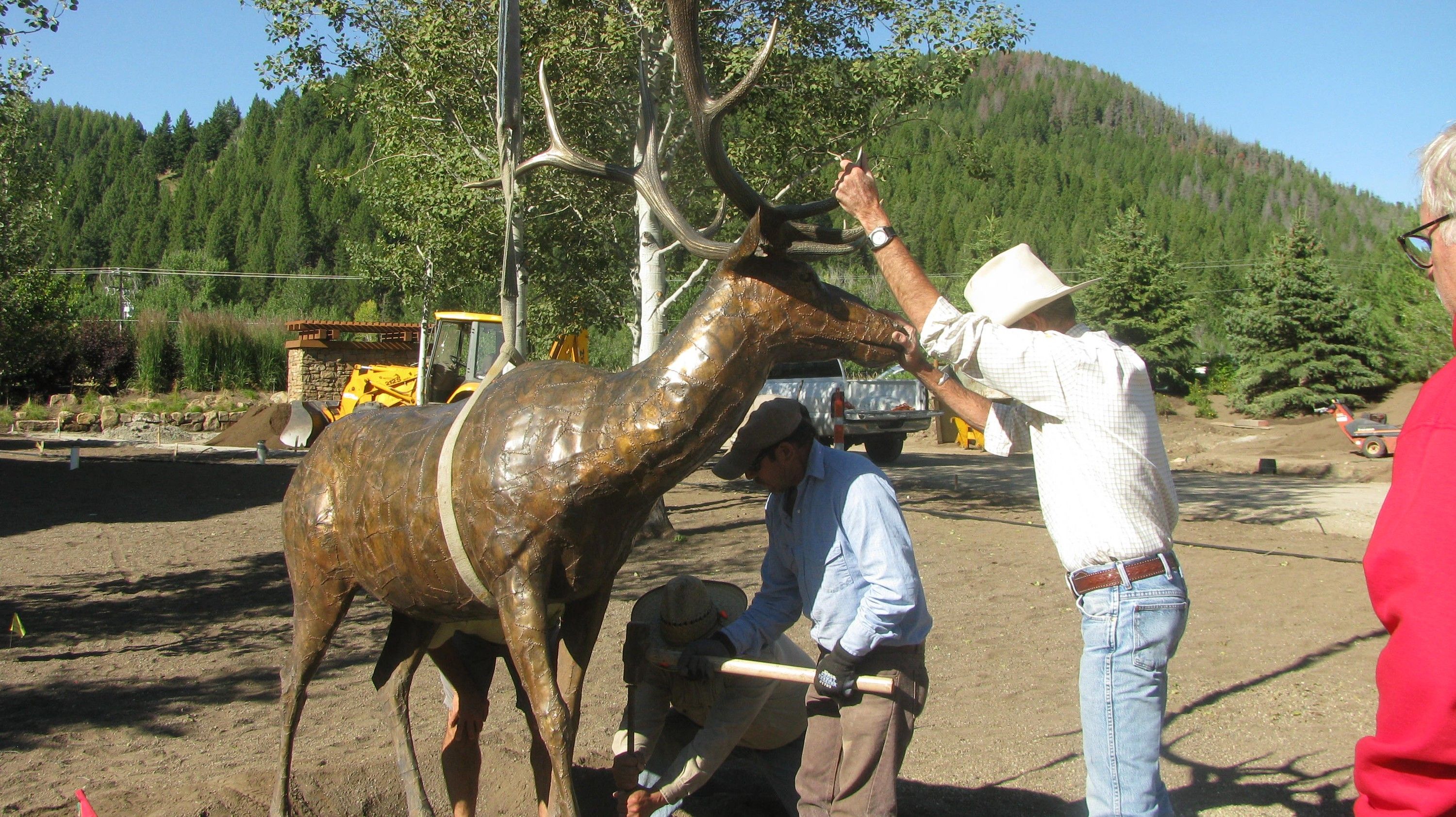Workers steadying the bronze bull elk by its antlers as it is set down on a graded site